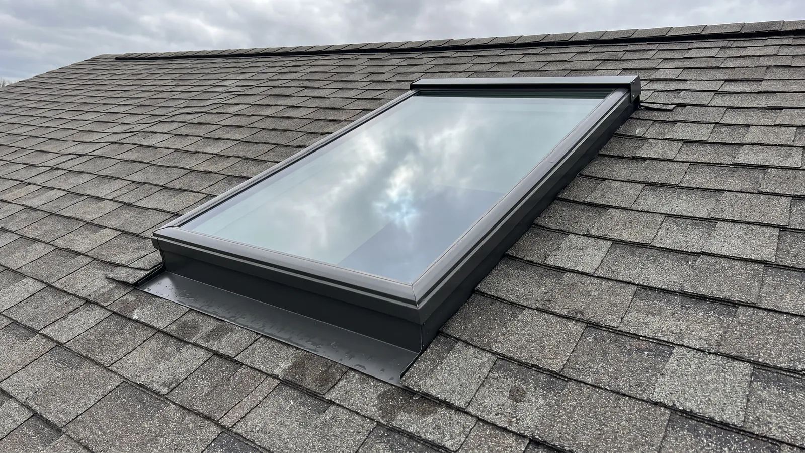 Newly installed skylight with its metal flashing kit set into an asphalt shingle roof